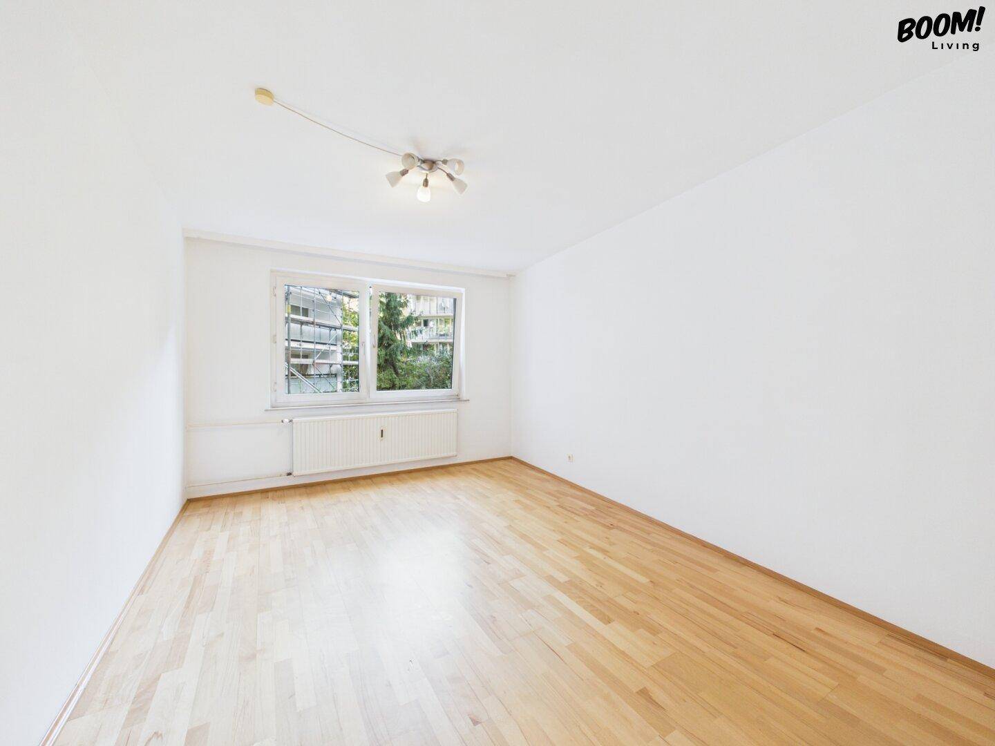 Helles Schlafzimmer mit Parkettboden und Fenster mit Blick ins Grüne.