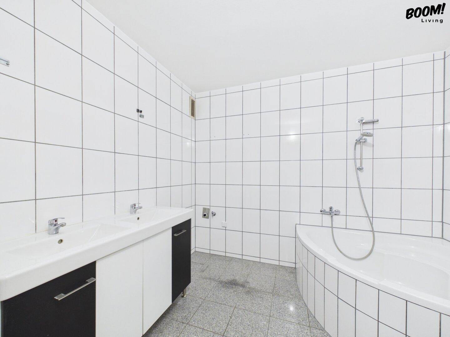 Badezimmer mit weißen Fliesen, Doppelwaschbecken und Eckbadewanne.