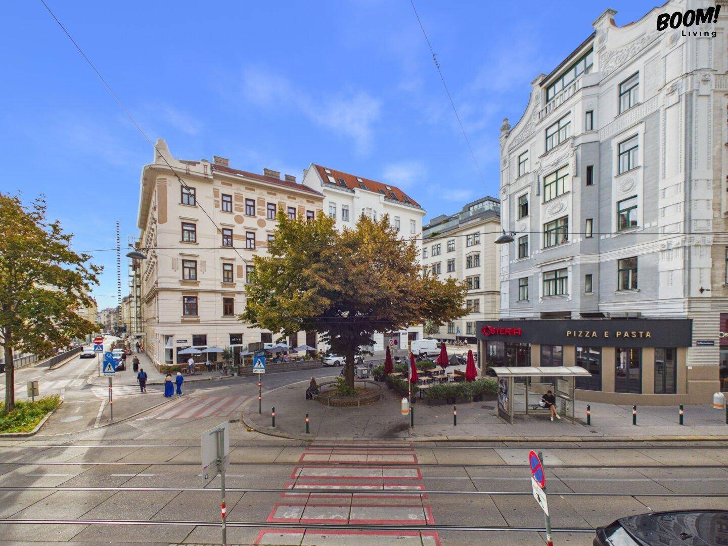 Stadtansicht mit Gebäuden, Straßenbahnlinien und einem belebten Platz mit Geschäften.