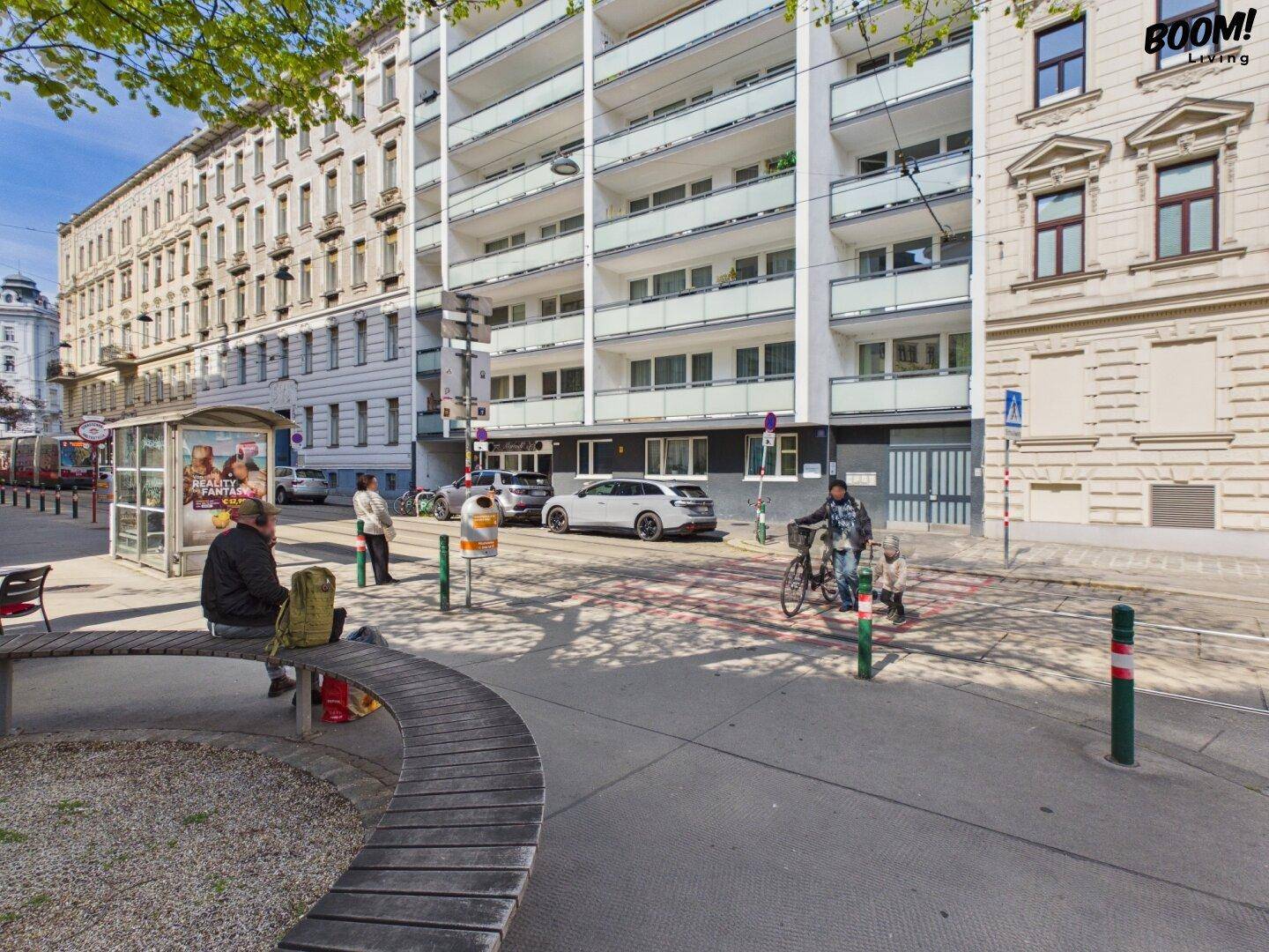 Straßenansicht mit Wohngebäuden, einer Bushaltestelle und einem Parkbereich.