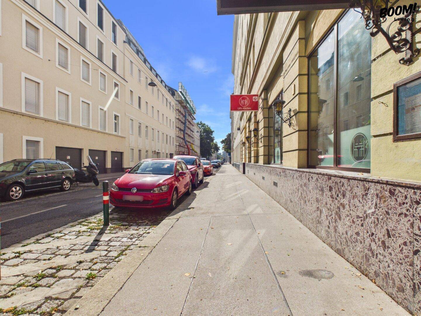 Städtische Straße mit geparkten Autos und Gebäuden unter blauem Himmel.