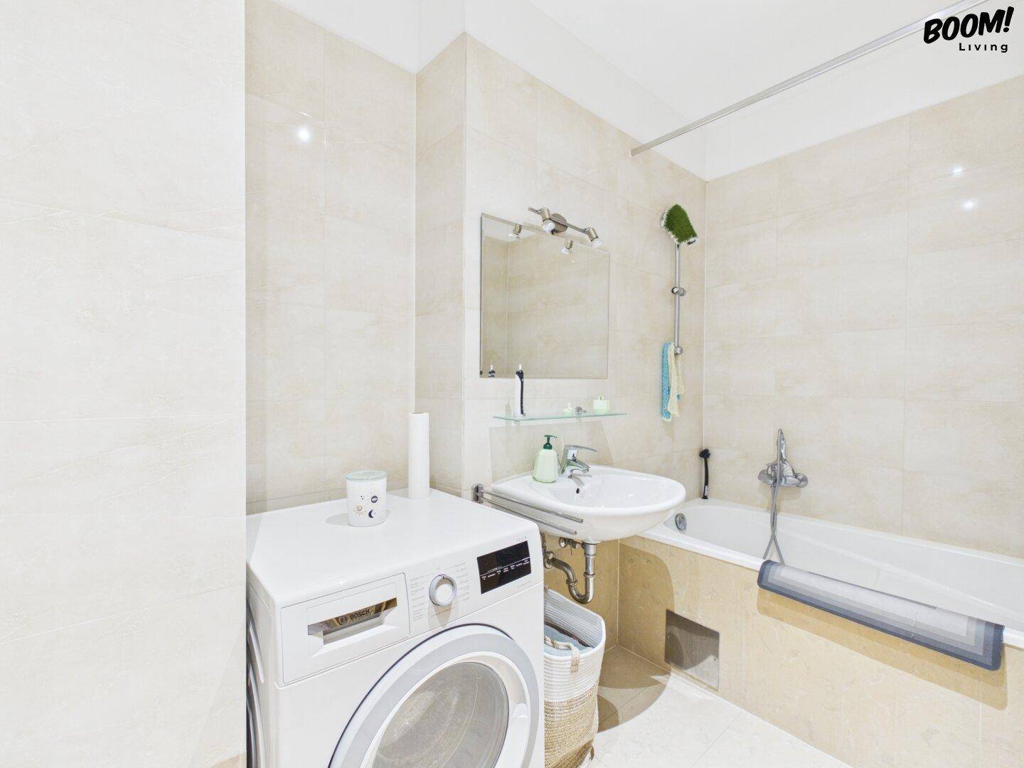 Modernes Badezimmer mit Badewanne, Waschbecken und Waschmaschine, hell gefliest.