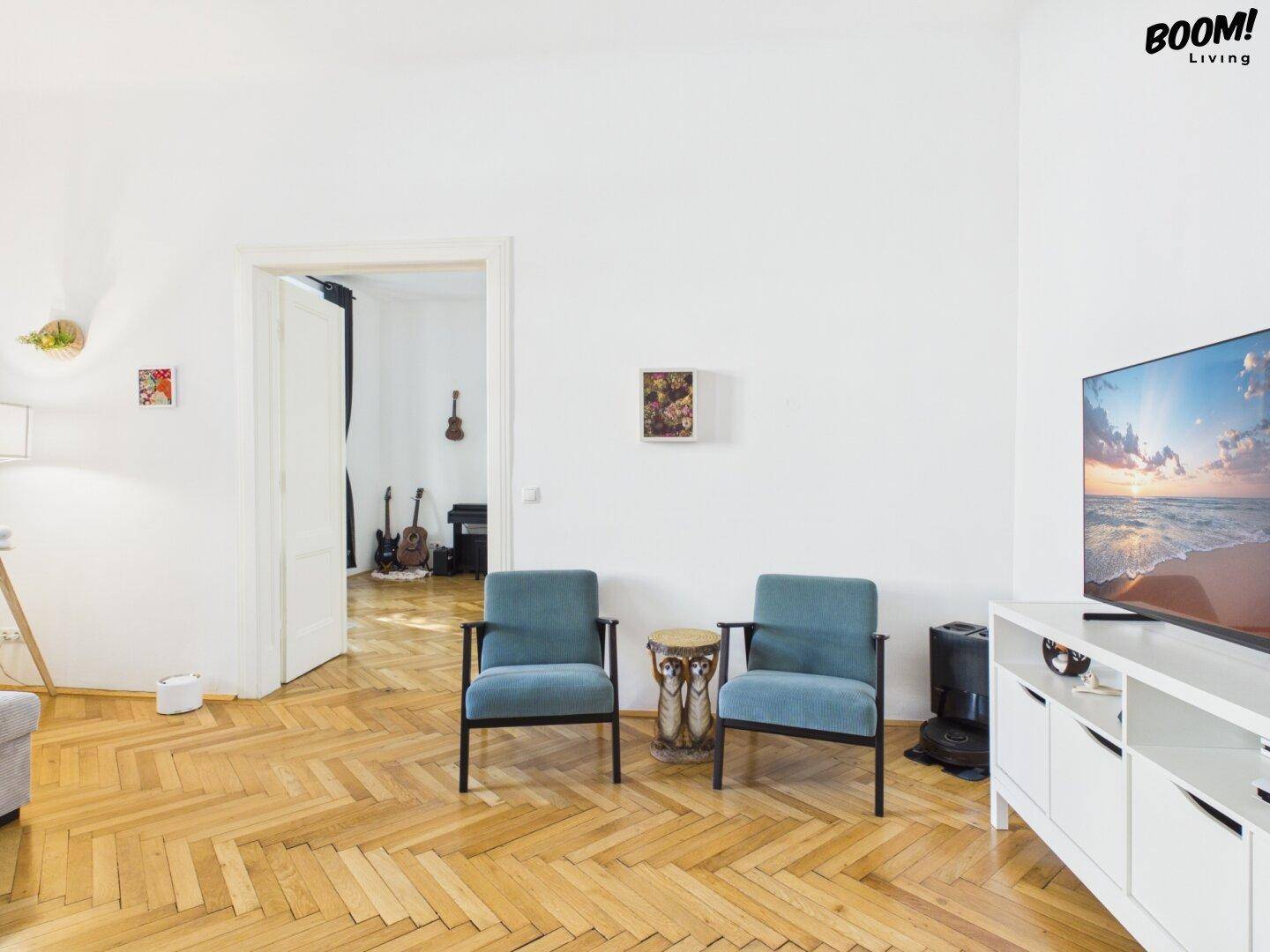 Gemütlicher Wohnbereich mit zwei Sesseln, Fernseher und klassischem Fischgrätparkett.