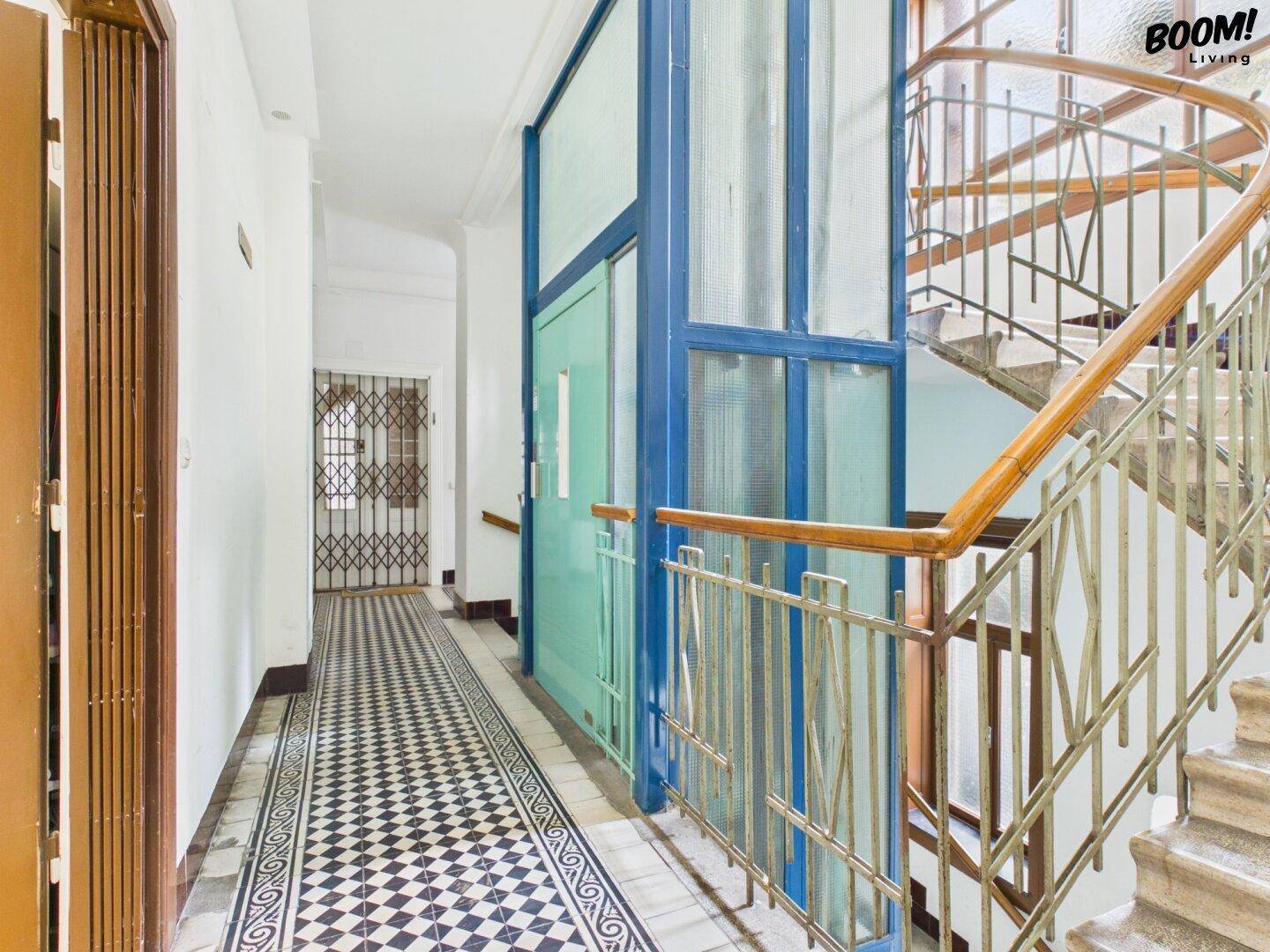 Historisches Treppenhaus mit Aufzug und gemusterten Bodenfliesen in einem Altbau.