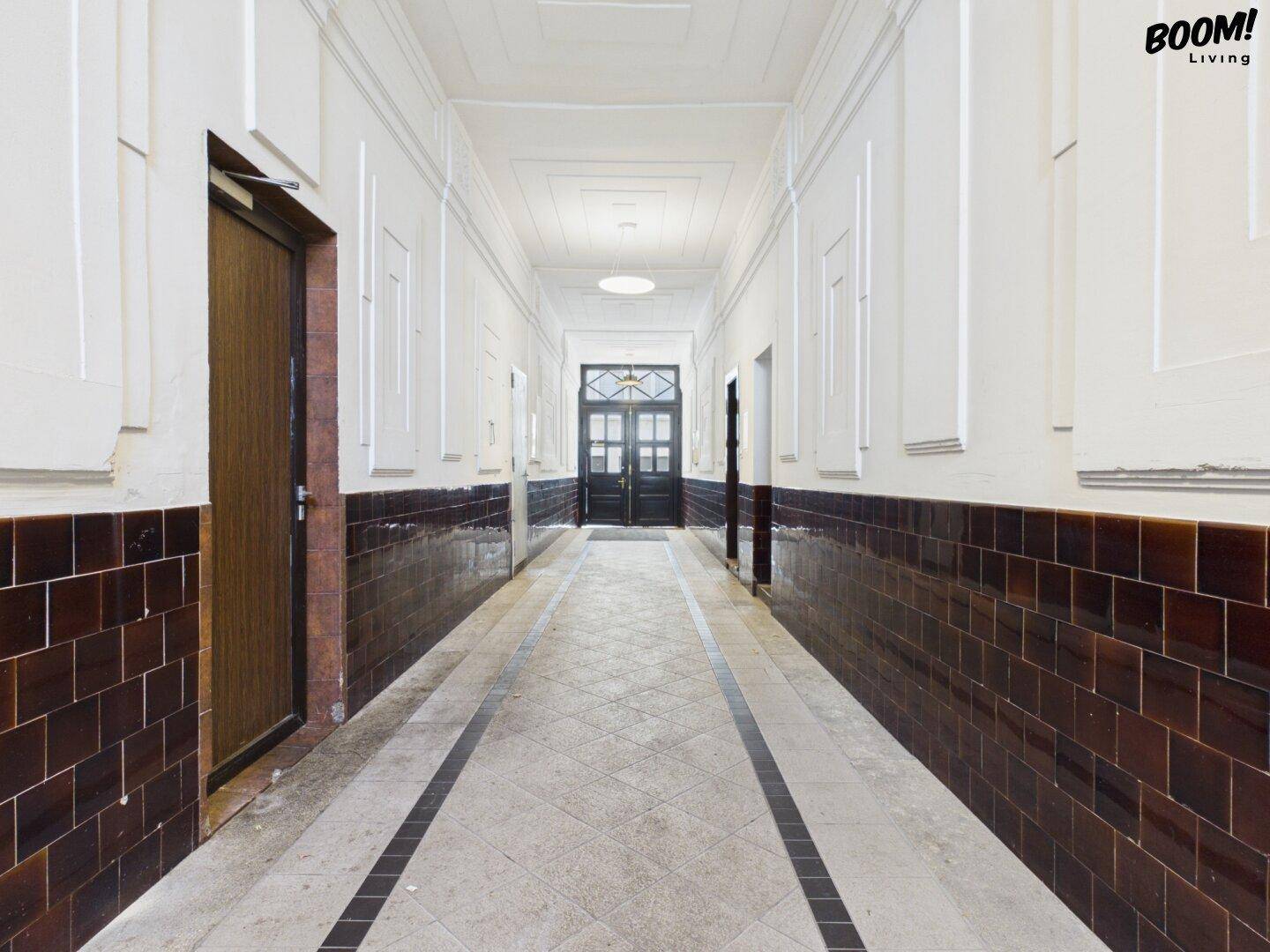 Langer, historischer Hausflur mit dunklen Fliesen und hohen Decken in einem Altbau.