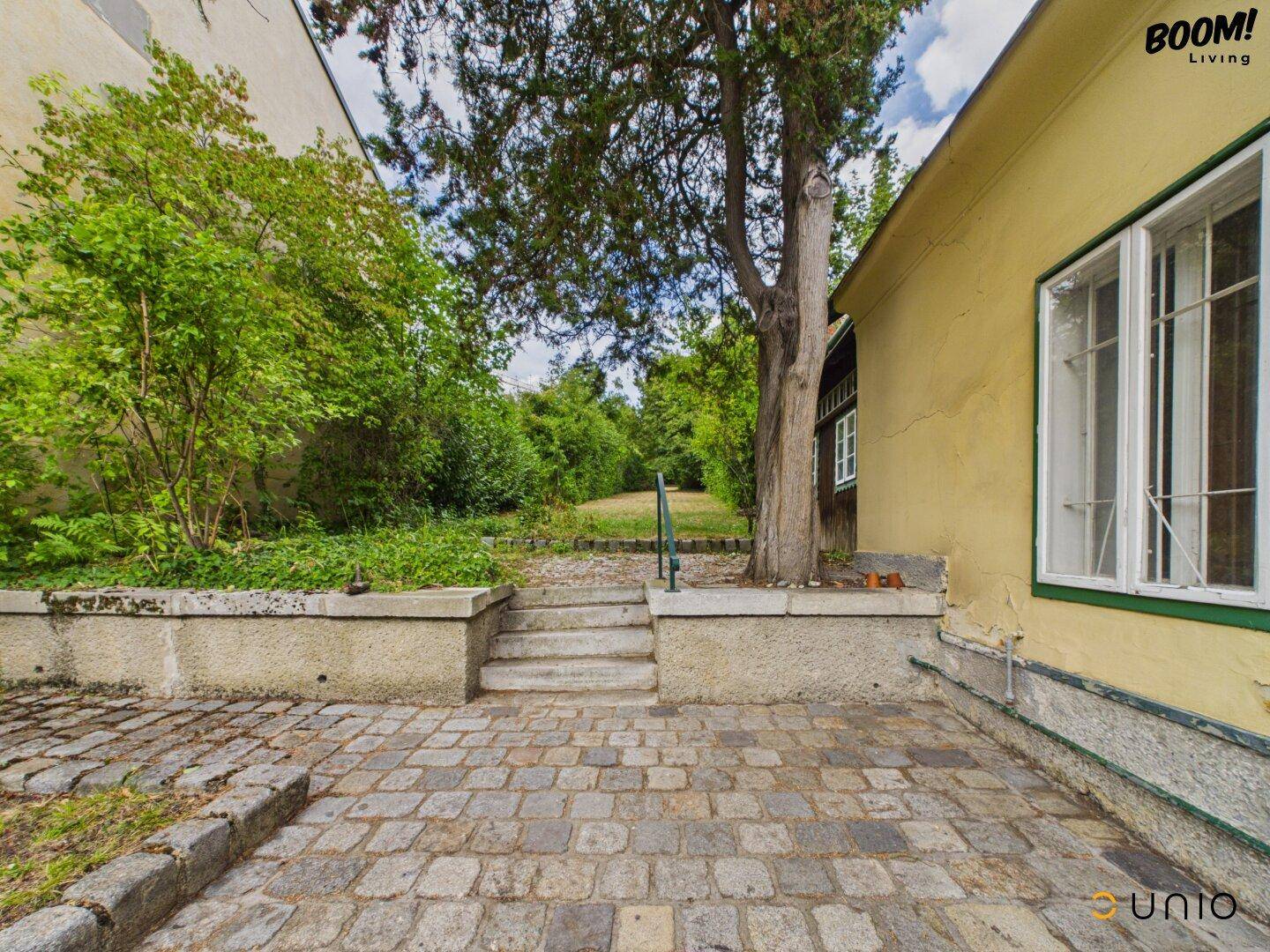 Gepflasterter Hofbereich mit Treppe, die zu einem höher gelegenen Garten führt.