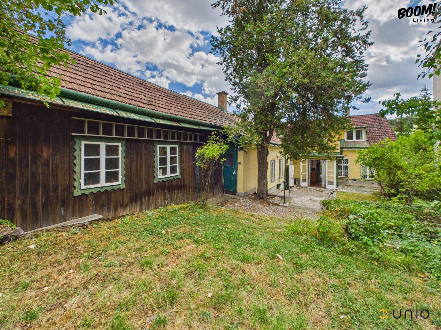 Rückseite des Holzgebäudes mit Gartenbereich und Blick auf das Hauptgebäude.