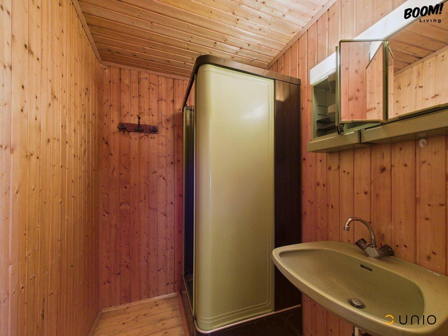 Kleines Badezimmer mit Holzverkleidung, Waschbecken, Spiegelschrank und Duschkabine.