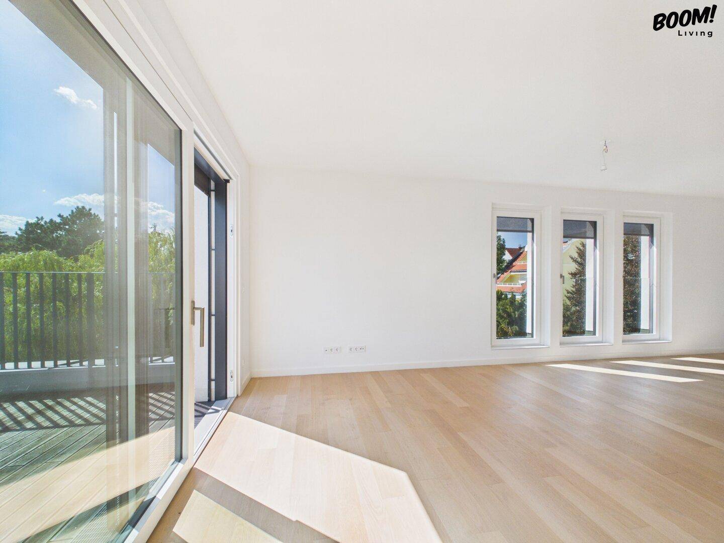 Helles Wohnzimmer mit Holzboden, großen Fenstern und Zugang zu einem Balkon.
