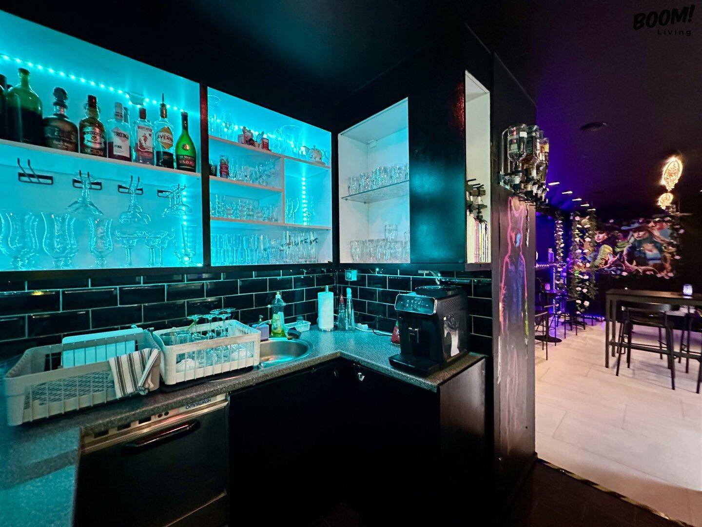 Moderne Bar mit blauer LED-Beleuchtung, gefüllten Regalen und dunklen Fliesen an der Wand.