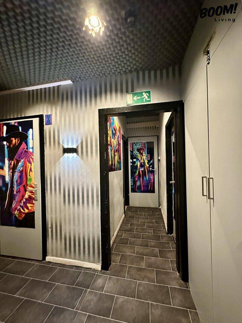 Flur mit dunklen Fliesen, modernen Wandleuchten und farbenfrohen Kunstwerken an den Türen.