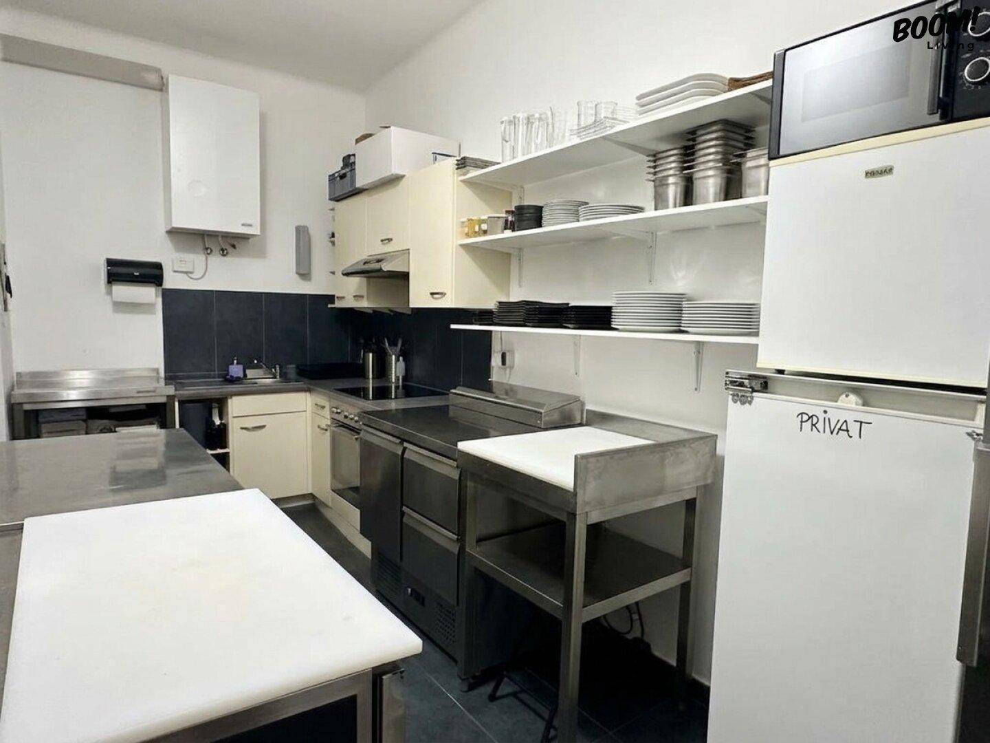 Geräumige Gewerbeküche mit Edelstahlgeräten, weißen Regalen und einem großen Kühlschrank.