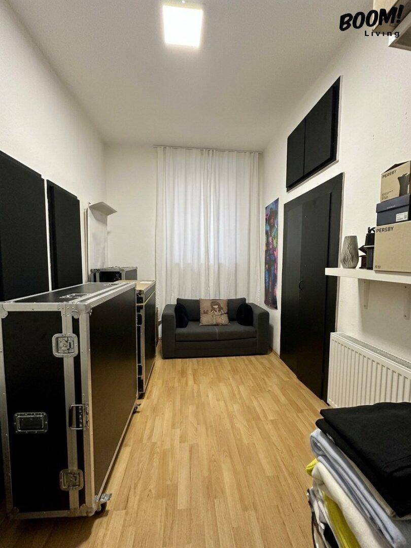 Schmaler Raum mit Holzboden, einem Sofa und schwarzen Akustikpaneelen an den Wänden.