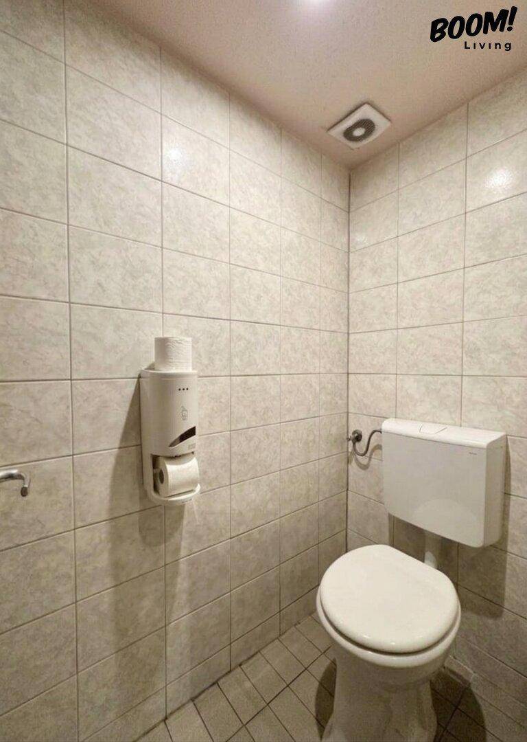 Einfache Toilette mit hellen Fliesen an Wänden und Boden, ausgestattet mit einem Spender.