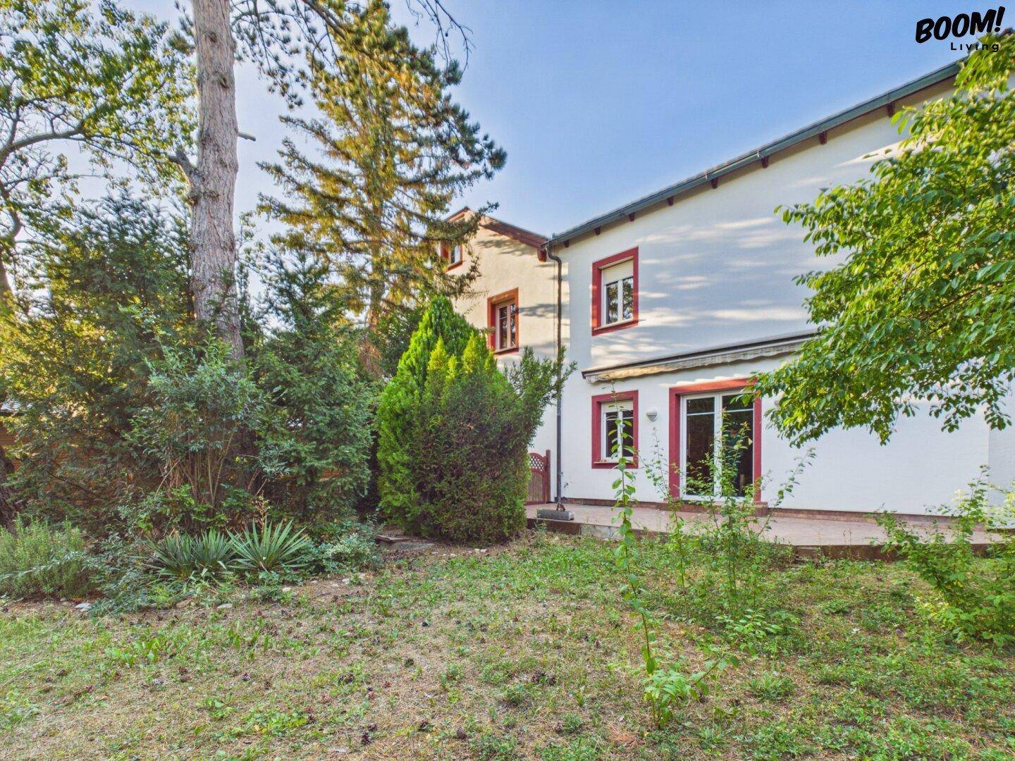 Rückseite des Hauses mit weißer Fassade und großen Fenstern, umgeben von einem grünen Garten.