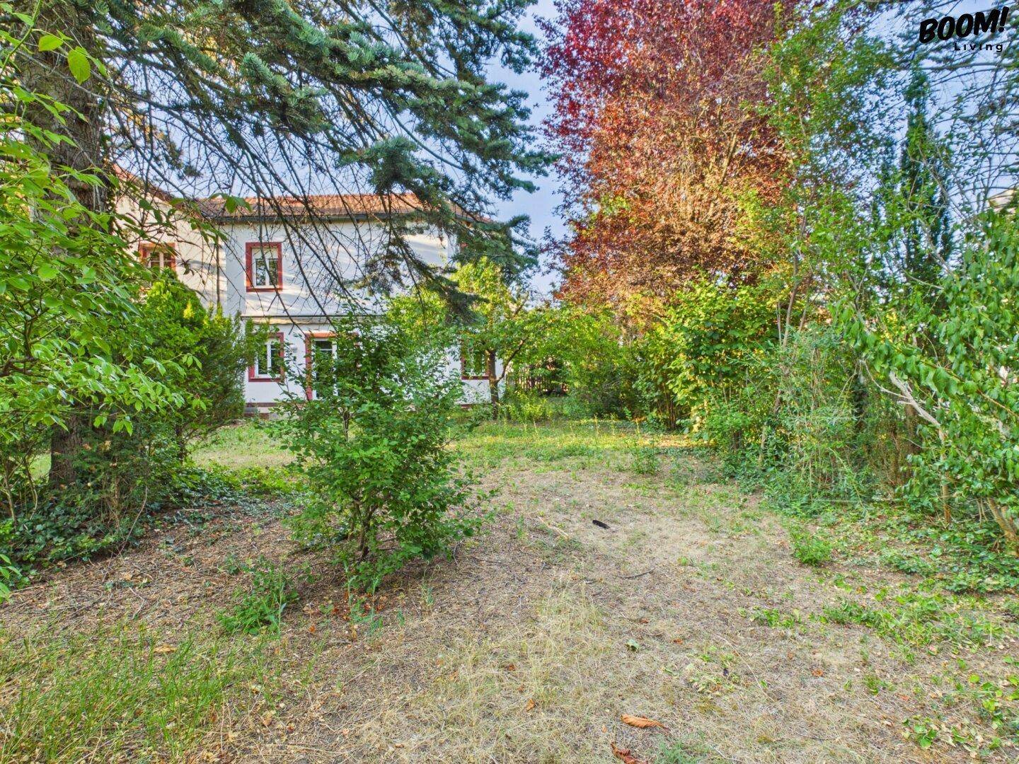 Gartenansicht des Hauses mit weißer Fassade und roten Akzenten, umgeben von üppigem Grün.