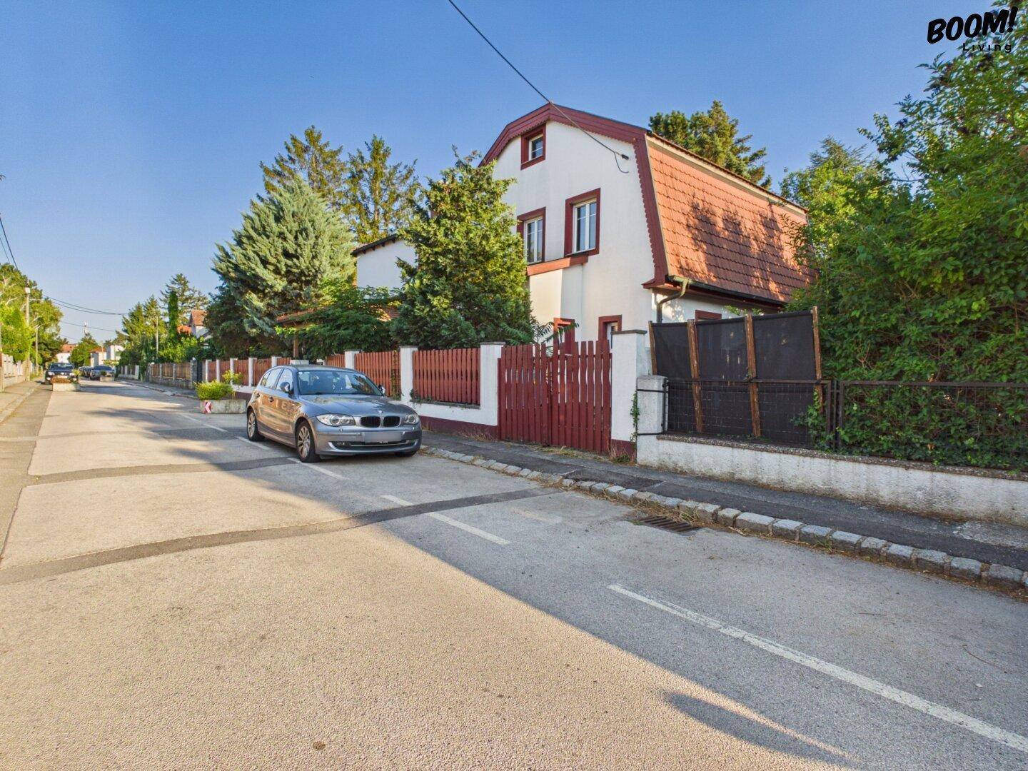 Seitenansicht des Hauses mit Mansarddach und umgebender Vegetation an einem sonnigen Tag.
