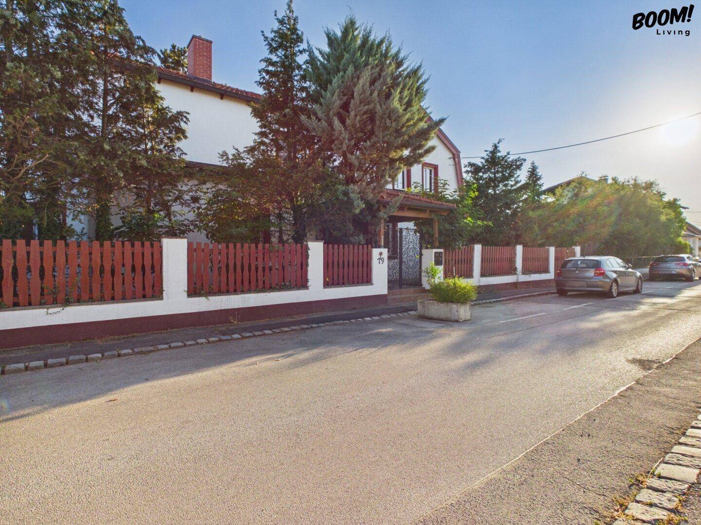 Seitenansicht des Hauses mit rotem Zaun und Bäumen, die das Grundstück umgeben.