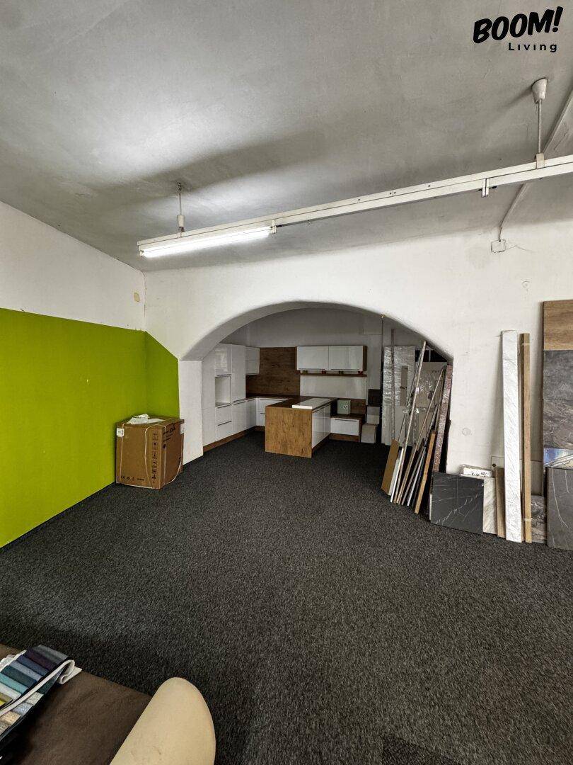 Großer offener Gewerberaum mit dunklem Teppichboden, grüner Akzentwand und einem Durchgang zu einer Küchenzeile.