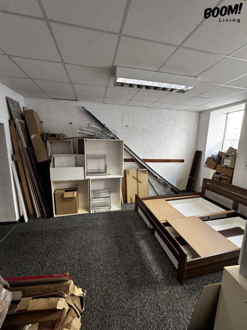 Lagerraum mit Teppichboden, abgehängter Decke und gestapelten Möbelteilen sowie Baumaterialien.