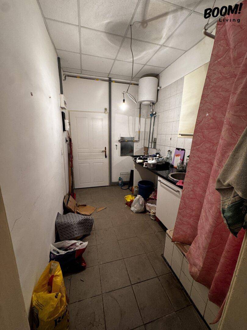 Kleine, unordentliche Küche mit Fliesenboden, weiß gefliesten Wänden, Spüle und Warmwasserboiler.