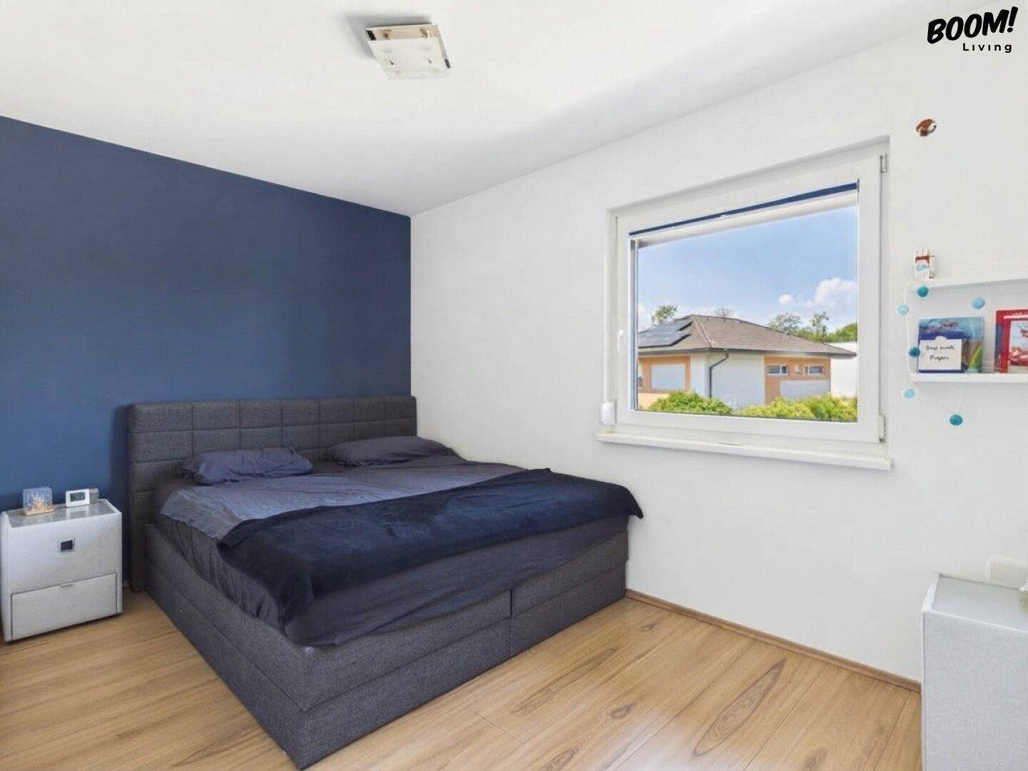 Gemütliches Schlafzimmer mit Doppelbett, blauer Akzentwand und hellem Holzfußboden.