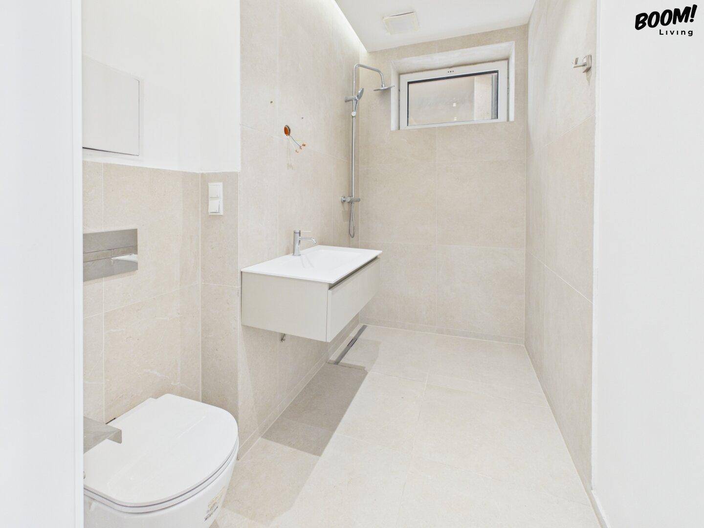 Modernes Badezimmer mit Dusche, wandhängendem WC und Fenster für natürliche Belüftung.