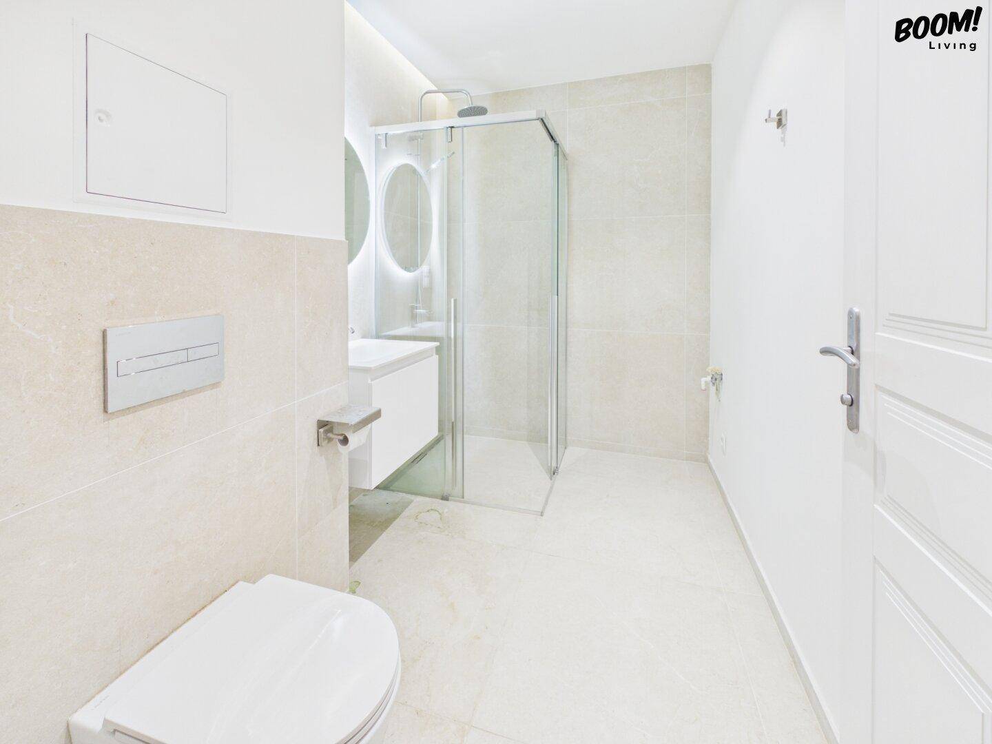 Helles Badezimmer mit großformatigen Fliesen, moderner Duschkabine und wandhängendem WC.