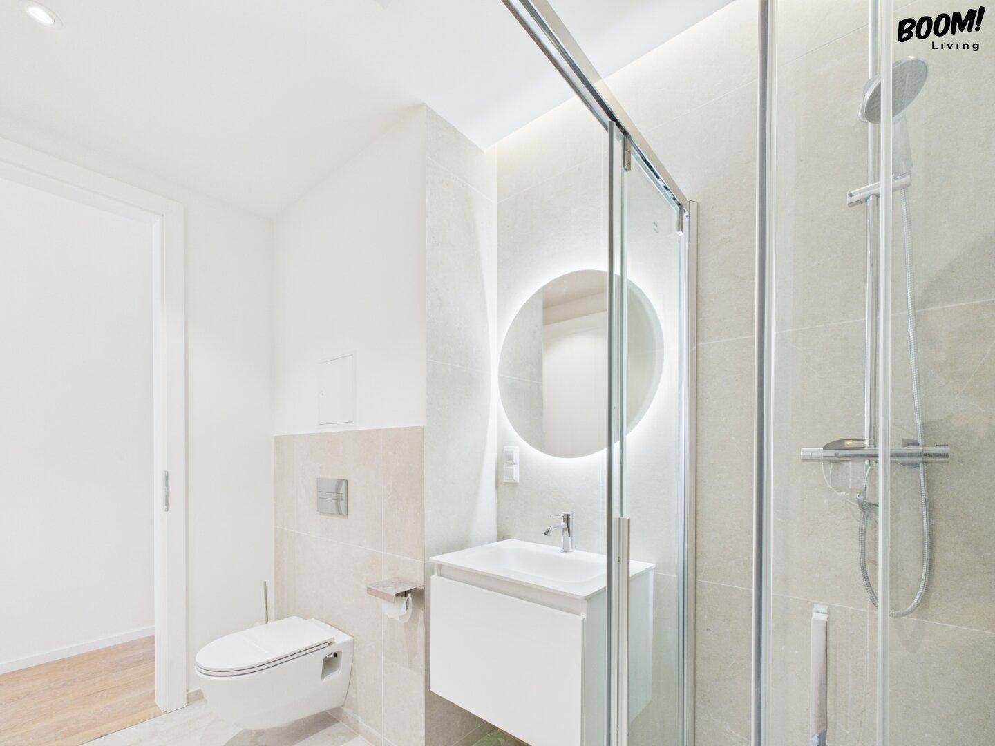 Modernes Badezimmer mit Duschkabine, wandhängendem WC und beleuchtetem Spiegel über dem Waschbecken.