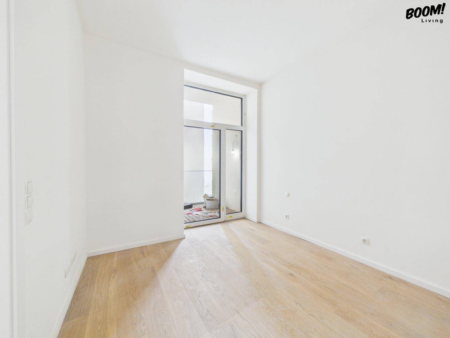 Heller Raum mit Holzboden und Zugang zu einem kleinen Balkon oder einer französischen Loggia.