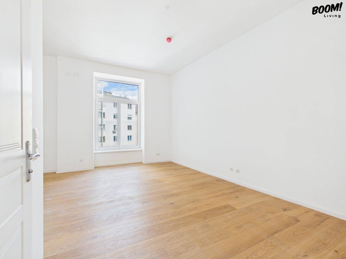 Heller Raum mit Holzboden und Fenster, das einen Blick auf die umliegenden Gebäude bietet.