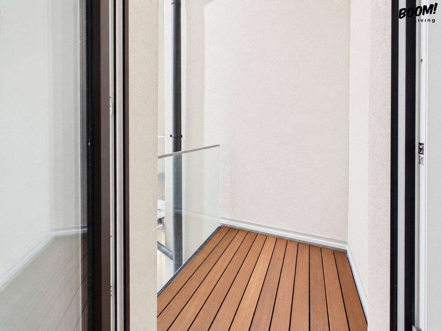 Kleiner Balkon mit Holzdielenboden und moderner Glasbrüstung, ideal für entspannte Stunden im Freien.