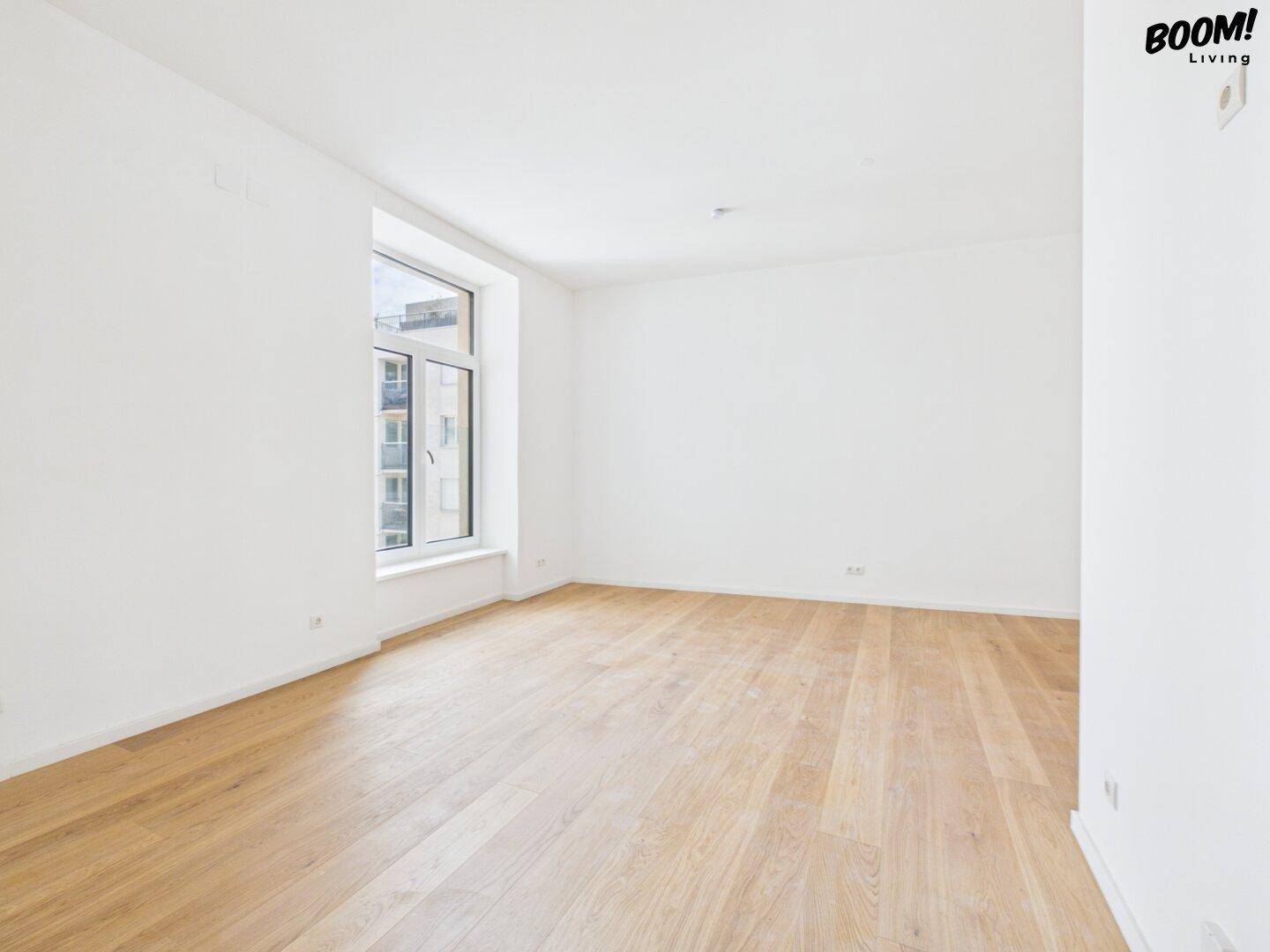 Heller, leerer Raum mit Eichenparkettboden und großem Fenster, ideal für ein Wohnzimmer.