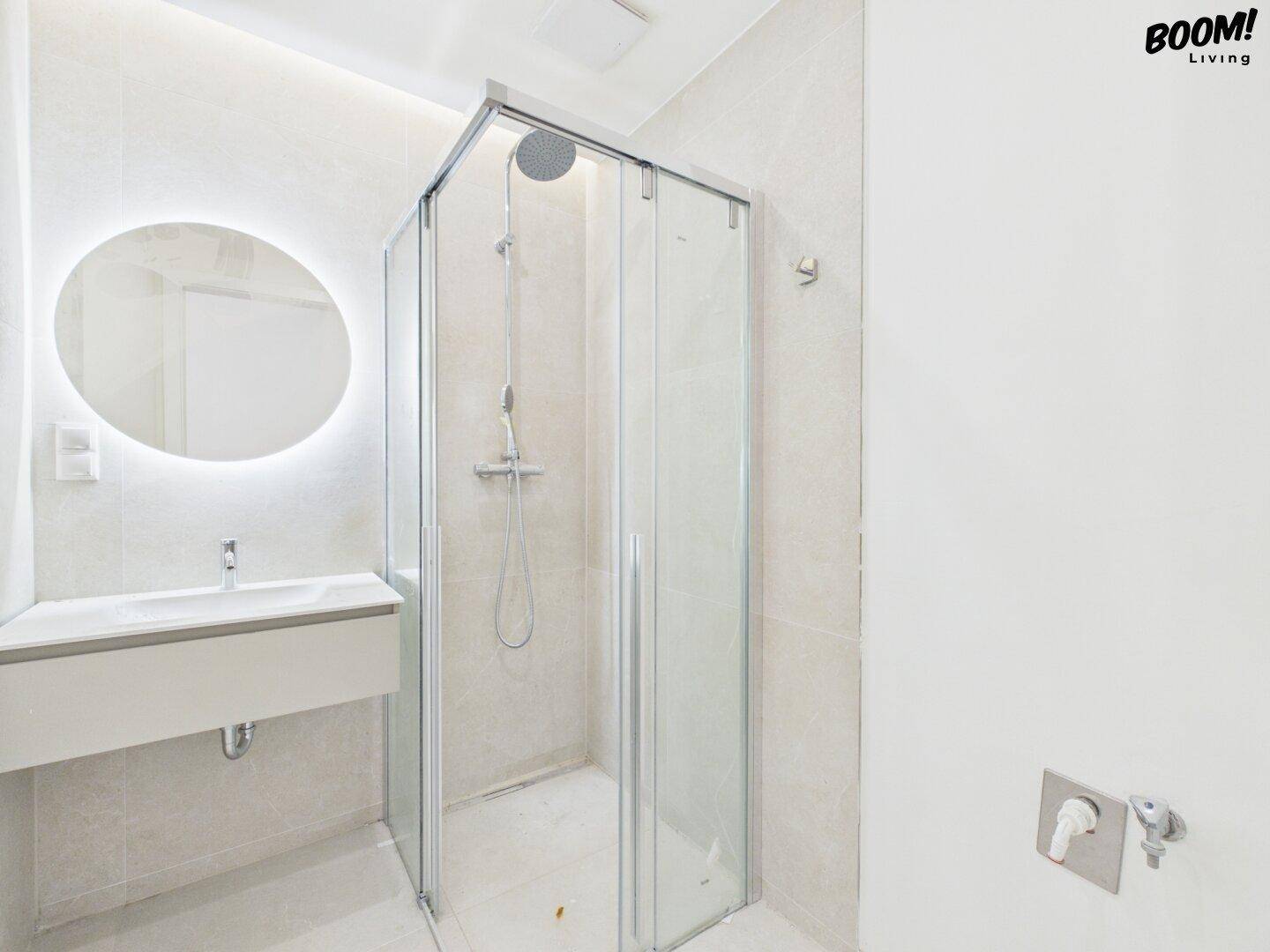 Modernes Badezimmer mit Duschkabine, beleuchtetem Spiegel und eleganten hellen Fliesen.