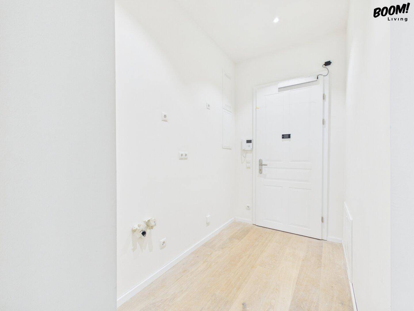Heller Eingangsbereich mit weißer Tür und hellem Holzfußboden, führt in weitere Räume der Wohnung.