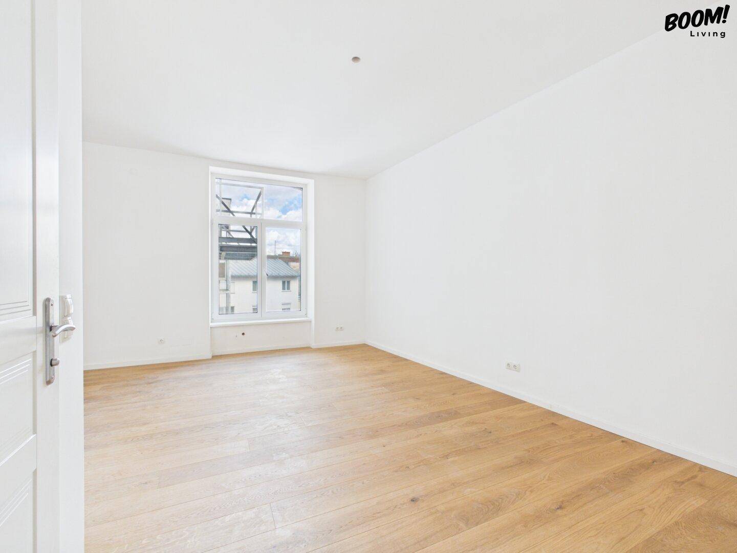 Unmöblierter Raum mit Holzboden und einem Fenster, das den Blick auf die Umgebung freigibt.