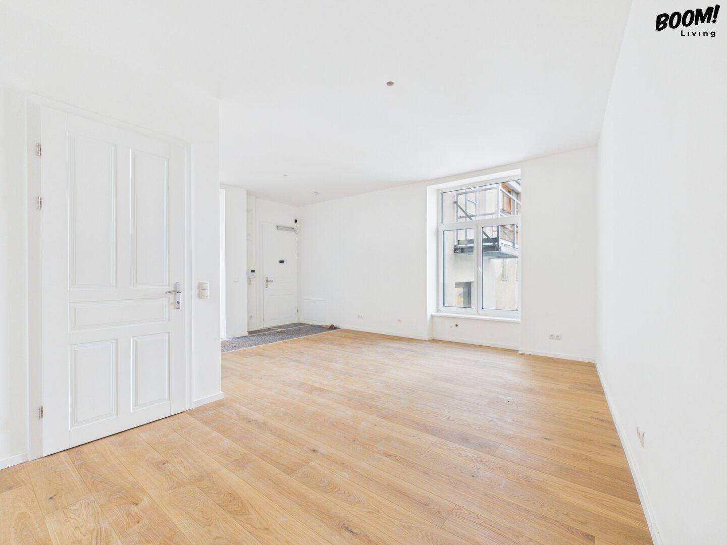 Geräumiger, heller Raum mit Holzboden und einem großen Fenster, das viel Tageslicht hereinlässt.