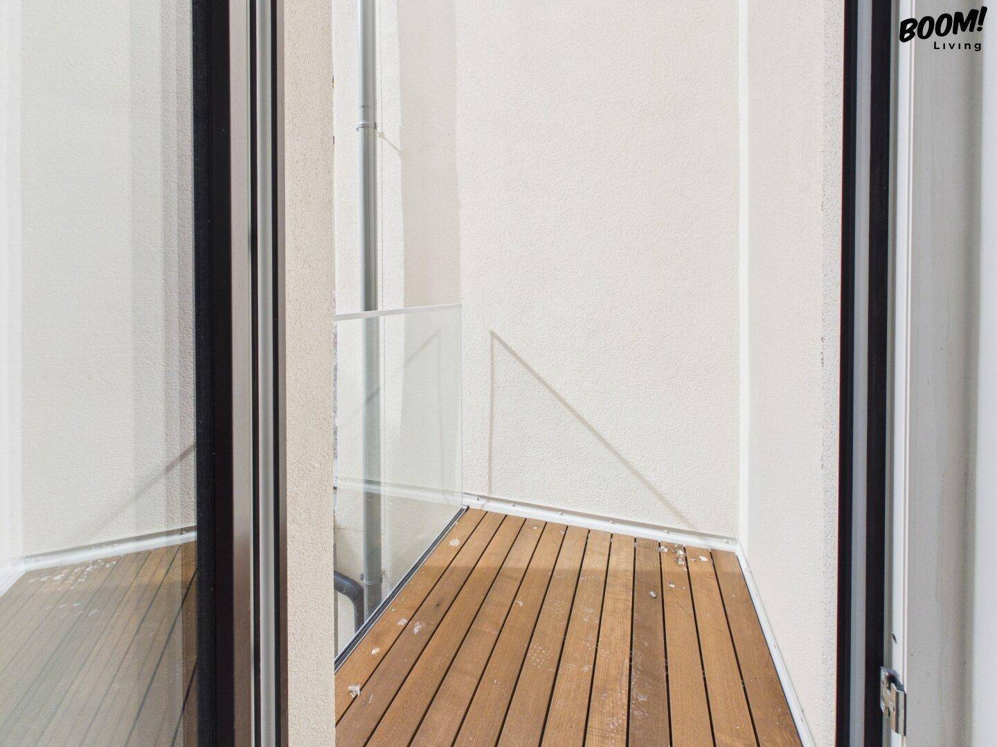Kleiner Balkon mit Holzboden und Glasbrüstung, ideal für eine kurze Auszeit im Freien.