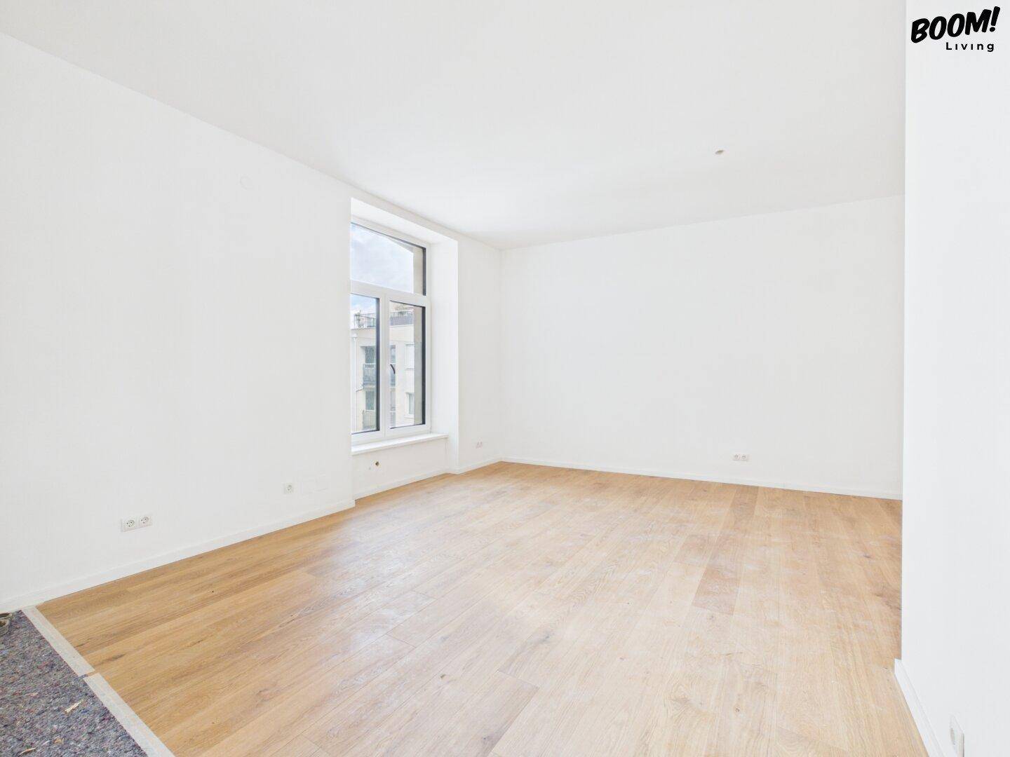 Leerer Raum mit hellem Parkettboden und einem großen Fenster, das eine angenehme Atmosphäre schafft.