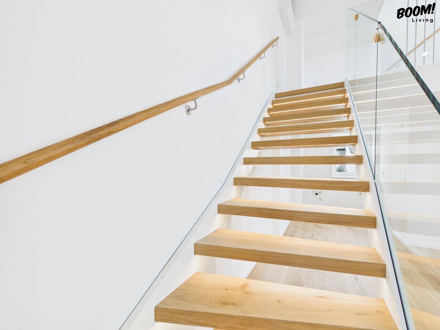 Moderne Holztreppe mit beleuchteten Stufen, Glasgeländer und elegantem Handlauf.