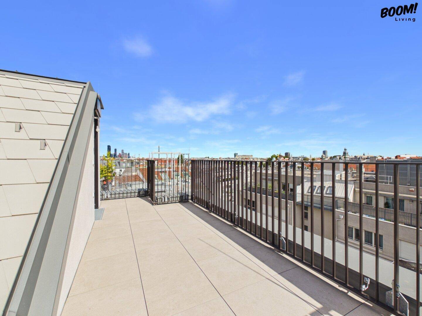 Weitläufige Dachterrasse mit Fliesenboden, Metallgeländer und Panoramablick über die Stadt.