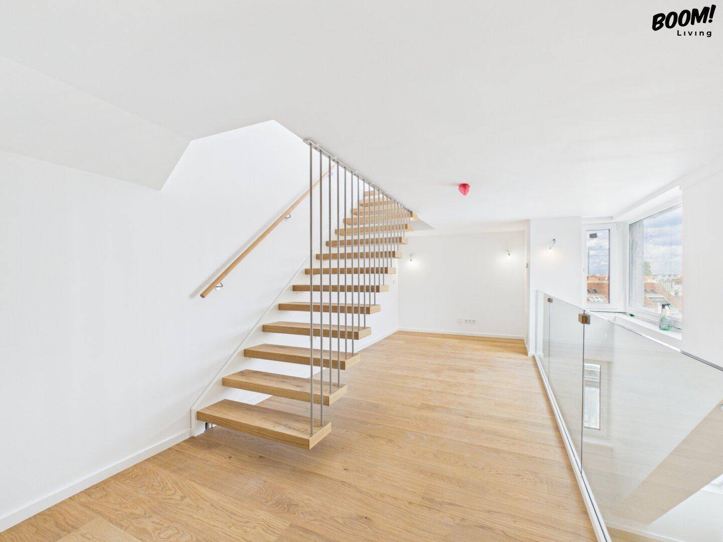 Heller Flurbereich im Obergeschoss mit Holzfußboden, moderner Treppe und Glasgeländer.