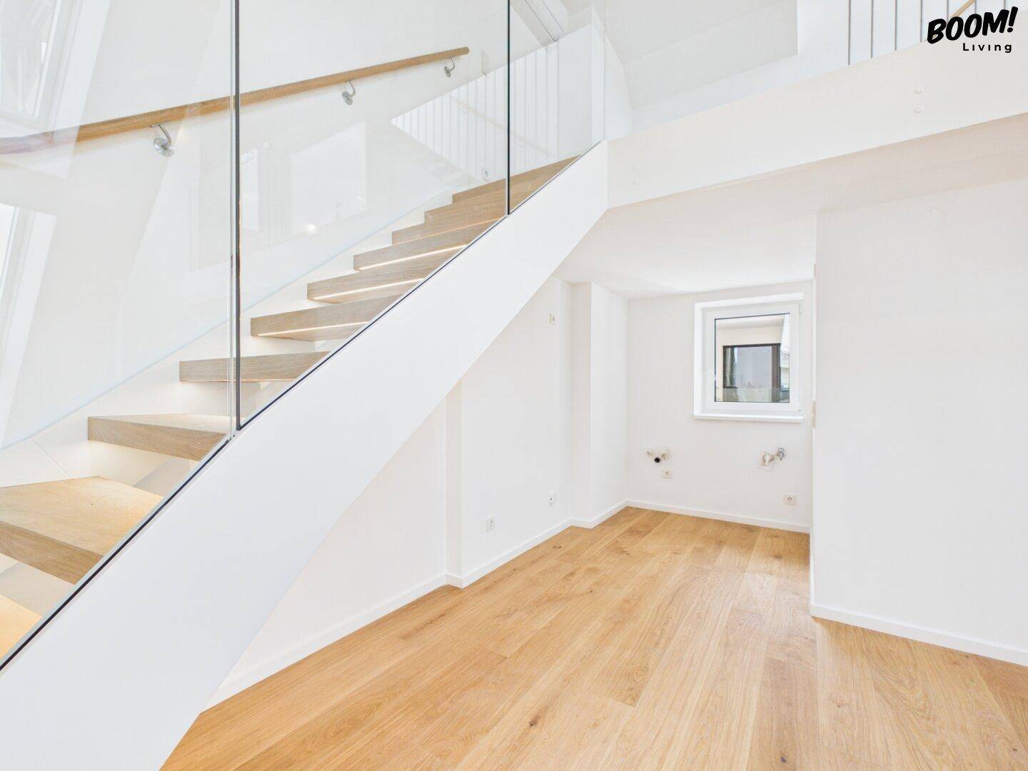 Leerer Raum mit Holzfußboden, Fenster und Anschlüssen, ideal für eine Küche oder einen Hauswirtschaftsraum.