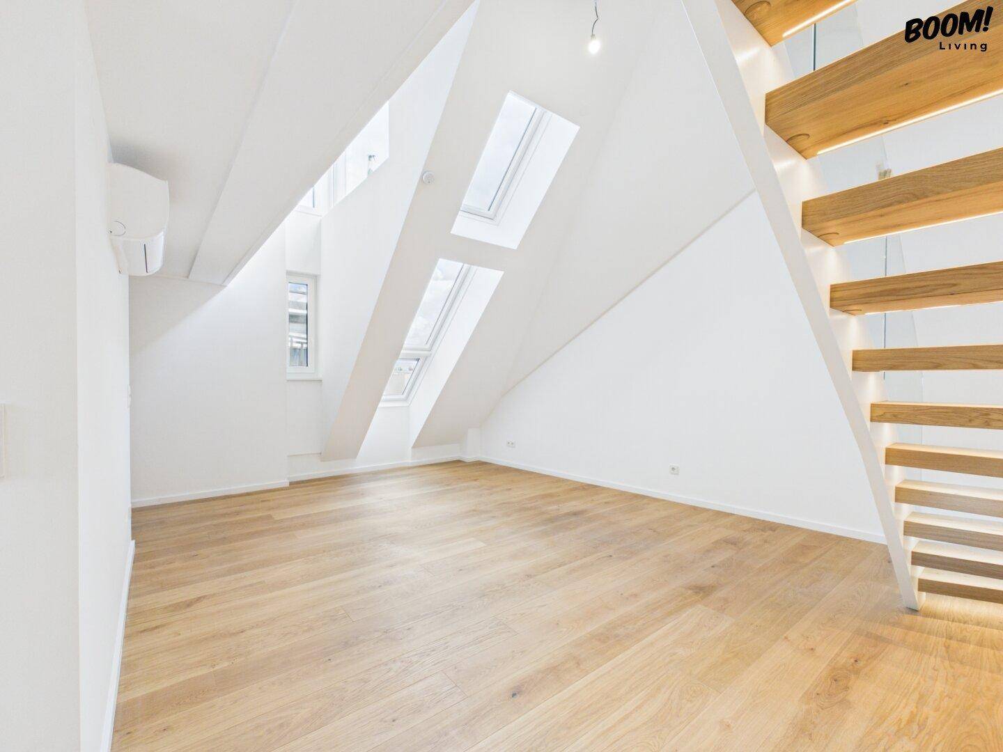 Heller Dachgeschossraum mit Holzfußboden, Dachschrägen und mehreren Dachfenstern.