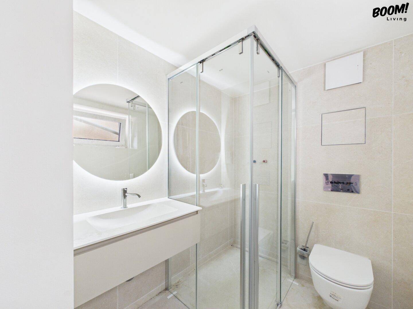 Modernes Badezimmer mit begehbarer Dusche, wandhängendem WC und beleuchtetem Spiegel.
