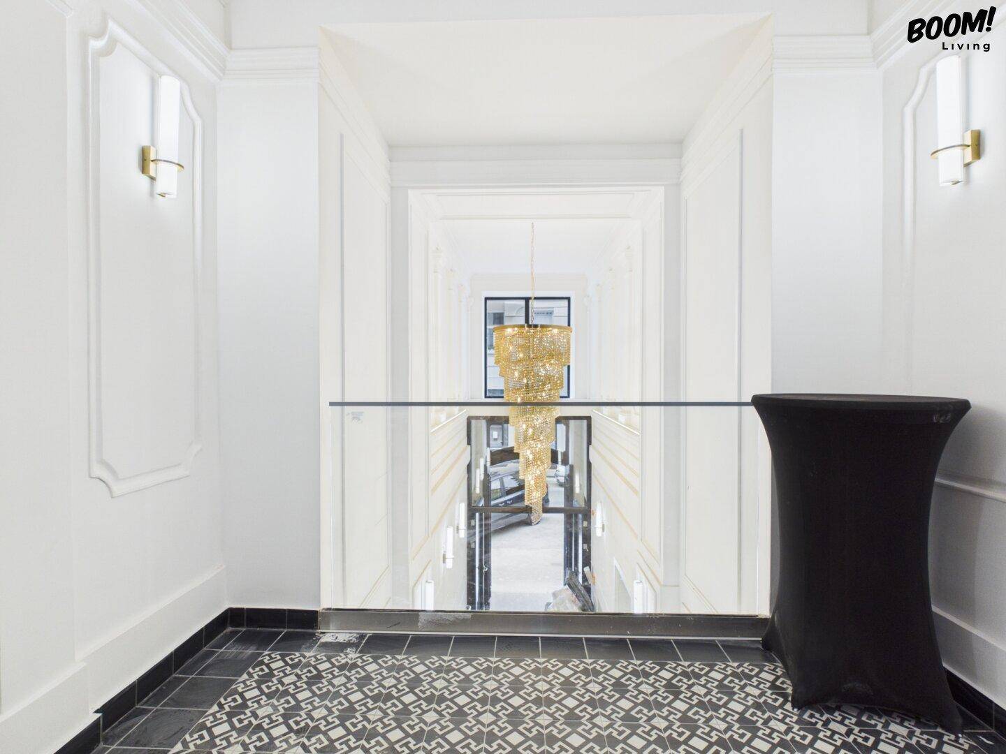 Blick von einer oberen Etage in den eleganten Flur mit modernem Kronleuchter und Glasgeländer.