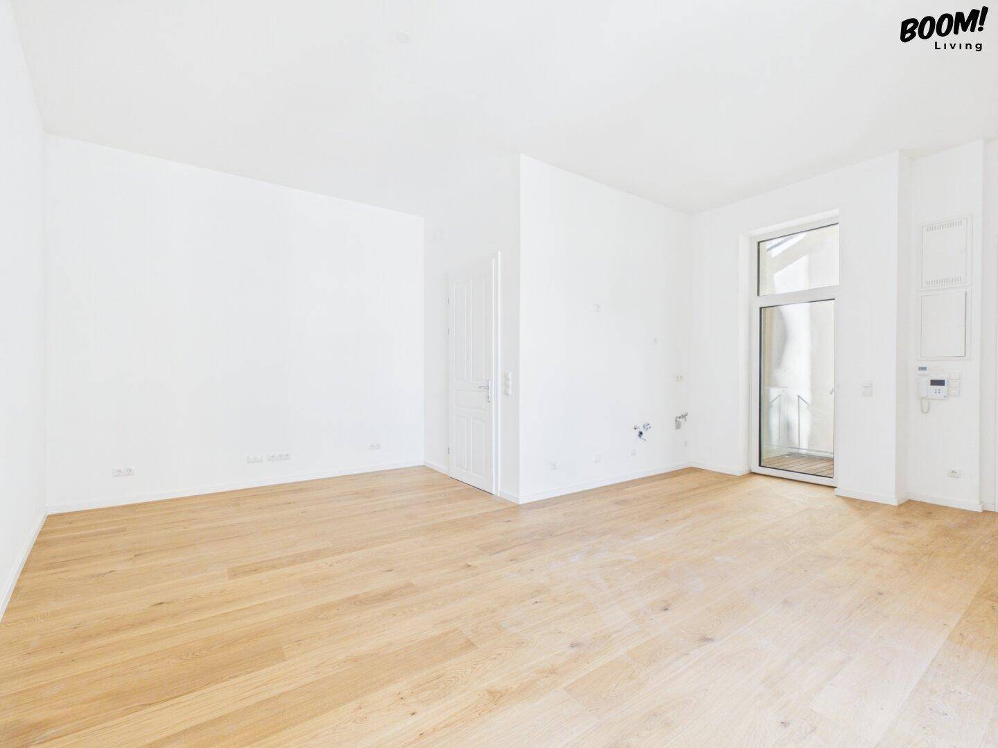 Heller, leerer Raum mit Holzboden und großem Fenster, bereit zur individuellen Gestaltung.