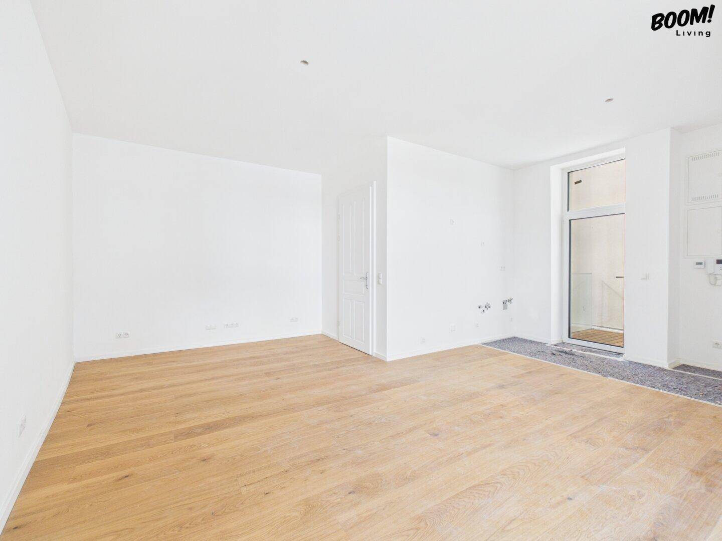 Heller, leerer Raum mit neuem Parkettboden und Zugang zu einem potenziellen Balkon oder Terrasse.