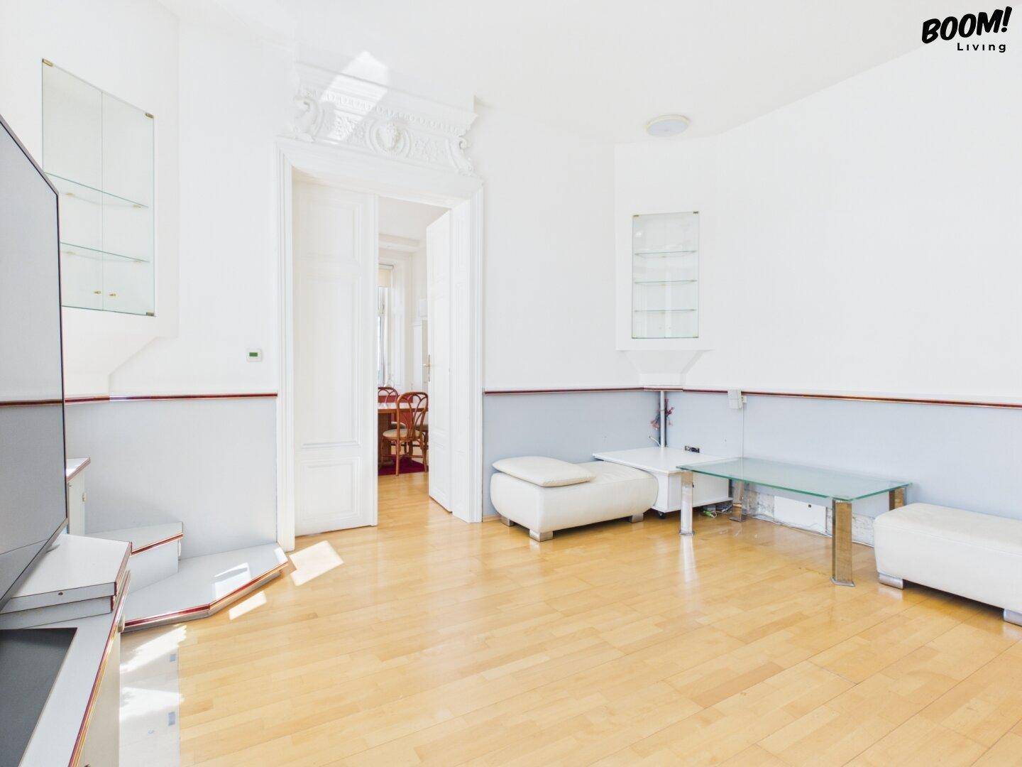Helles Wohnzimmer mit Parkettboden, minimalistischen Möbeln und Blick in den Essbereich.
