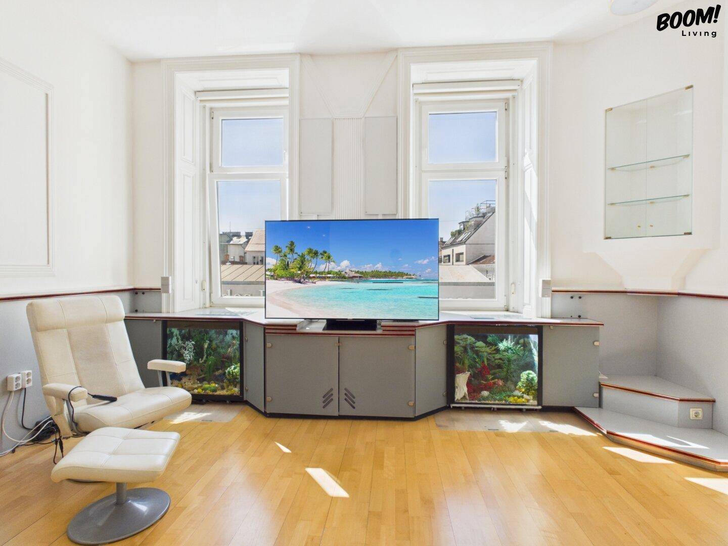 Wohnzimmer mit Parkettboden, Sessel und großen Fenstern mit Stadtblick.
